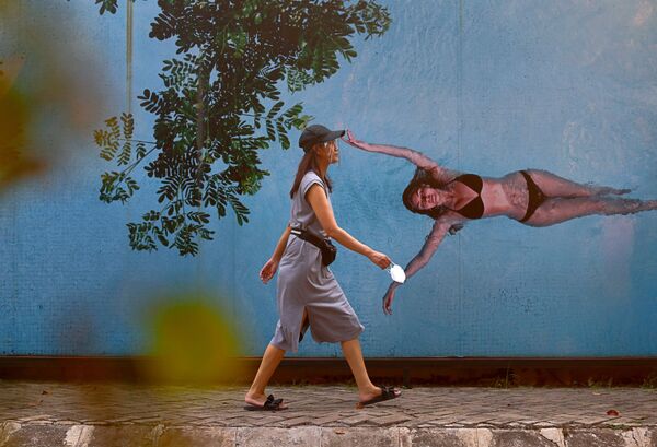Một cô gái đeo khẩu trang bảo vệ trên nền tranh graffiti mô tả cô gái mặc đồ bơi ở Jakarta, Indonesia - Sputnik Việt Nam