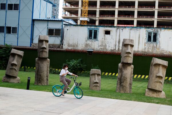 Cô gái đi xe đạp trước các bản sao tượng đá Moai ở khu thương mại Bắc Kinh - Sputnik Việt Nam