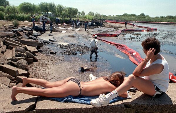Những người đi nghỉ bên cạnh công nhân khi họ dọn dẹp bãi biển chứa dầu ở Argentina, 1999 - Sputnik Việt Nam