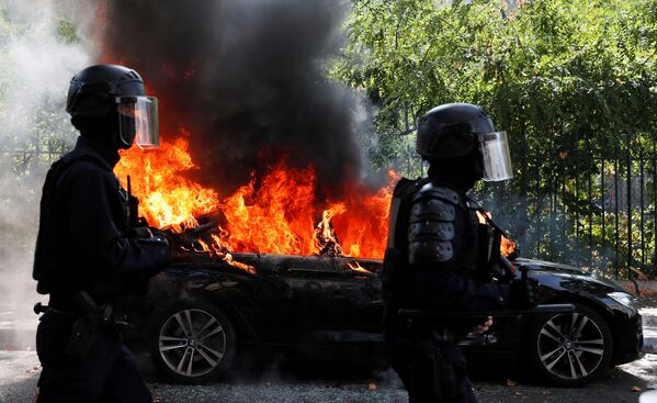 Cảnh sát Pháp đi ngang qua chiếc ô tô bốc cháy trong cuộc biểu tình ủng hộ phong trào Áo vàng ở Paris - Sputnik Việt Nam
