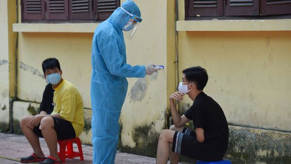 Nhân viên y tế mặc quần áo bảo hộ kiểm tra thân nhiệt của một người ở Hà Nội. - Sputnik Việt Nam