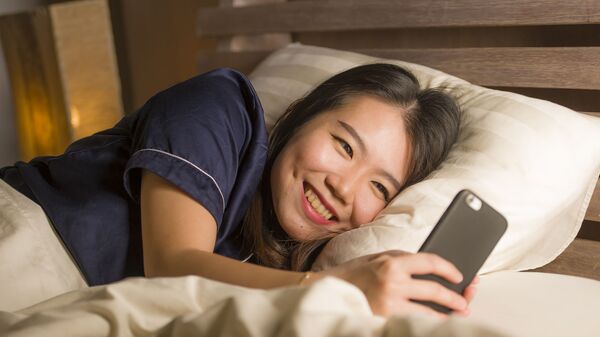 Cô gái Nhật Bản trẻ tuổi đang cười khi sử dụng điện thoại thông minh - Sputnik Việt Nam