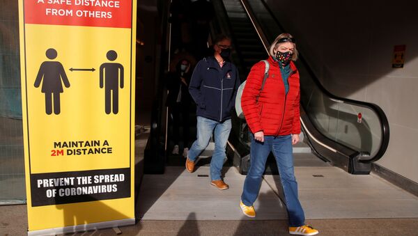 Những người đeo mặt nạ bảo hộ đi ngang qua một biển báo ngăn cách xã hội ở Coventry, Vương quốc Anh - Sputnik Việt Nam