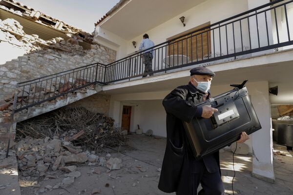 Một người đàn ông với chiếc TV bên ngoài ngôi nhà bị hư hỏng sau trận động đất ở Hy Lạp - Sputnik Việt Nam