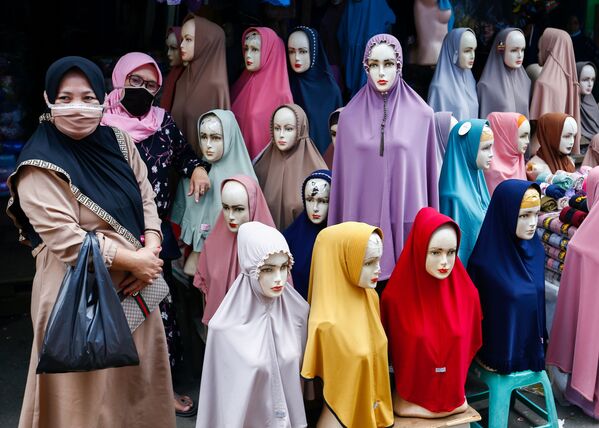 Những người phụ nữ đeo khẩu trang đứng cạnh những chiếc khăn trùm đầu được bày bán tại chợ dệt may Tanah Abang ở Jakarta, Indonesia. - Sputnik Việt Nam