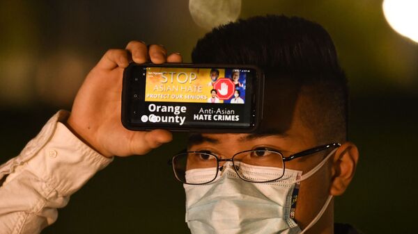 Một người đàn ông cầm điện thoại với thông điệp về tội ác căm thù đối với người Mỹ gốc Á trong một cuộc đấu trí ở Fountain Valley, California - Sputnik Việt Nam