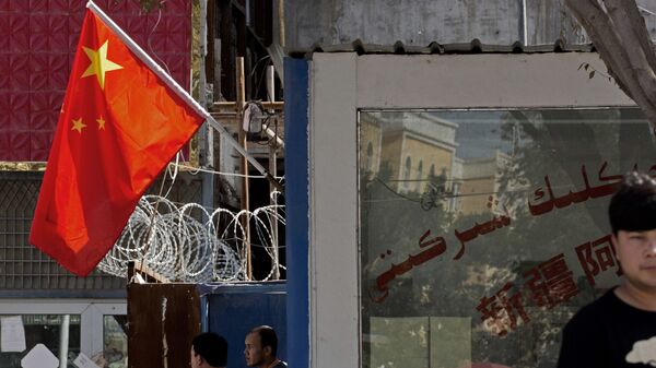 Người dân đứng gần hàng rào có dây thép gai và quốc kỳ Trung Quốc ở khu vực Tân Cương, miền tây Trung Quốc. - Sputnik Việt Nam