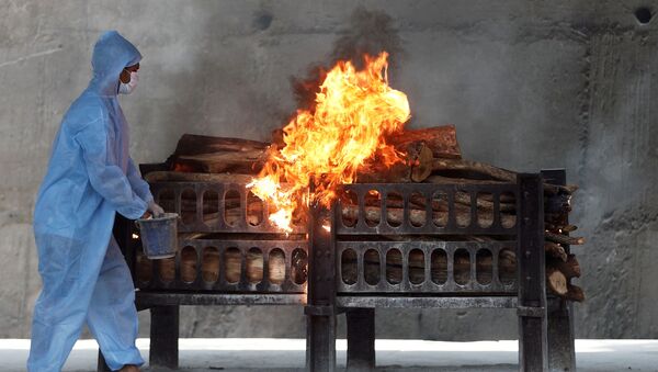 Công nhân mặc thiết bị bảo hộ cá nhân phun chất lỏng dễ cháy lên giàn hỏa táng xác người đàn ông chết vì COVID-19, Ấn Độ. - Sputnik Việt Nam
