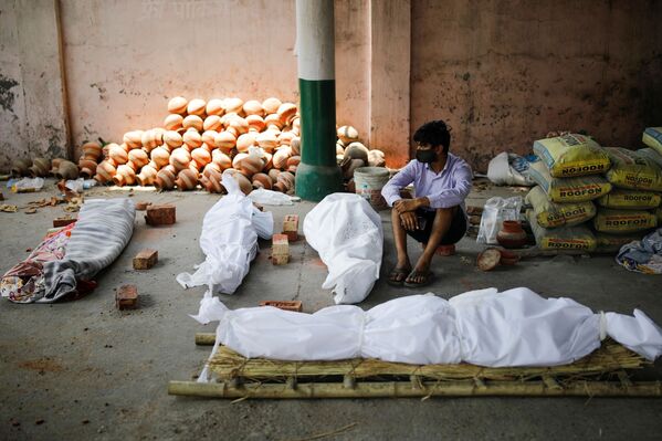 Người đàn ông ngồi bên cạnh thi thể của những người chết vì COVID trước khi thiêu xác hàng loạt tại nhà hỏa táng ở New Delhi, Ấn Độ - Sputnik Việt Nam