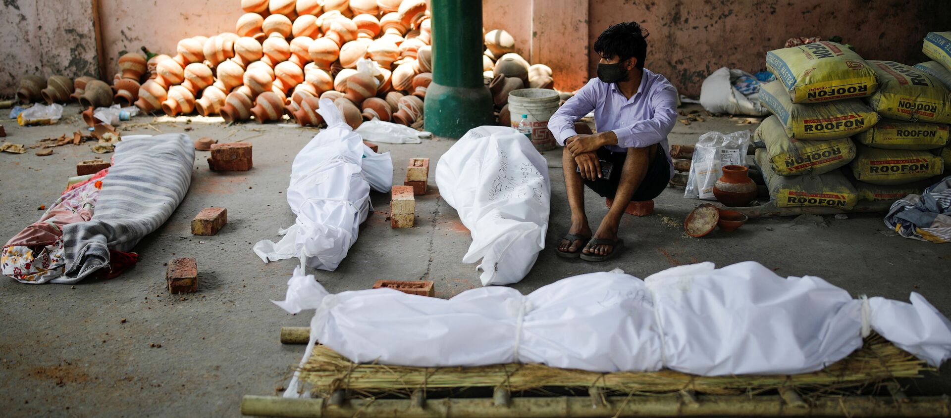 Người đàn ông ngồi bên cạnh thi thể của những người chết vì COVID trước khi thiêu xác hàng loạt tại nhà hỏa táng ở New Delhi, Ấn Độ - Sputnik Việt Nam, 1920, 12.05.2021