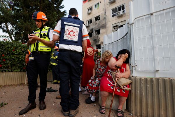 Các nhân viên y tế Israel đứng cạnh những người phụ nữ gần ngôi nhà bị hư hại ở Ashkelon do tên lửa phóng từ Dải Gaza  - Sputnik Việt Nam