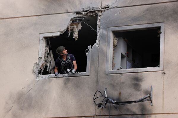 Chuyên gia xử lý bom mìn của cảnh sát Israel nhìn ra cửa sổ tòa chung cư bị hư hại ở Ashkelon do tên lửa phóng từ Dải Gaza - Sputnik Việt Nam