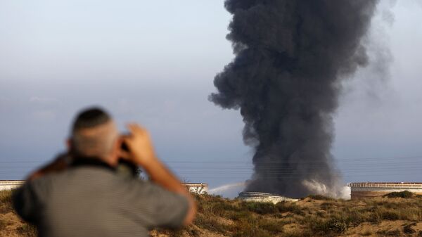 Một người đàn ông Israel nhìn từ xa khi khói bốc lên vào sáng sớm ngày 12 tháng 5 năm 2021 từ nhà máy lọc dầu của Ashkelon, bị trúng tên lửa Hamas vào ngày hôm trước, ở thành phố phía nam Israel, gần Dải Gaza - Sputnik Việt Nam