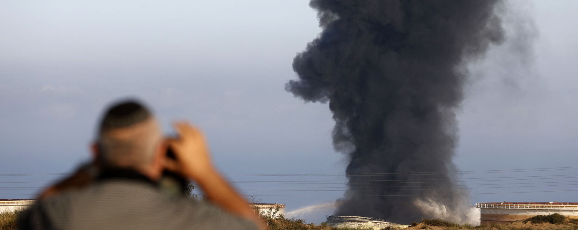 Một người đàn ông Israel nhìn từ xa khi khói bốc lên vào sáng sớm ngày 12 tháng 5 năm 2021 từ nhà máy lọc dầu của Ashkelon, bị trúng tên lửa Hamas vào ngày hôm trước, ở thành phố phía nam Israel, gần Dải Gaza - Sputnik Việt Nam, 1920, 13.05.2021