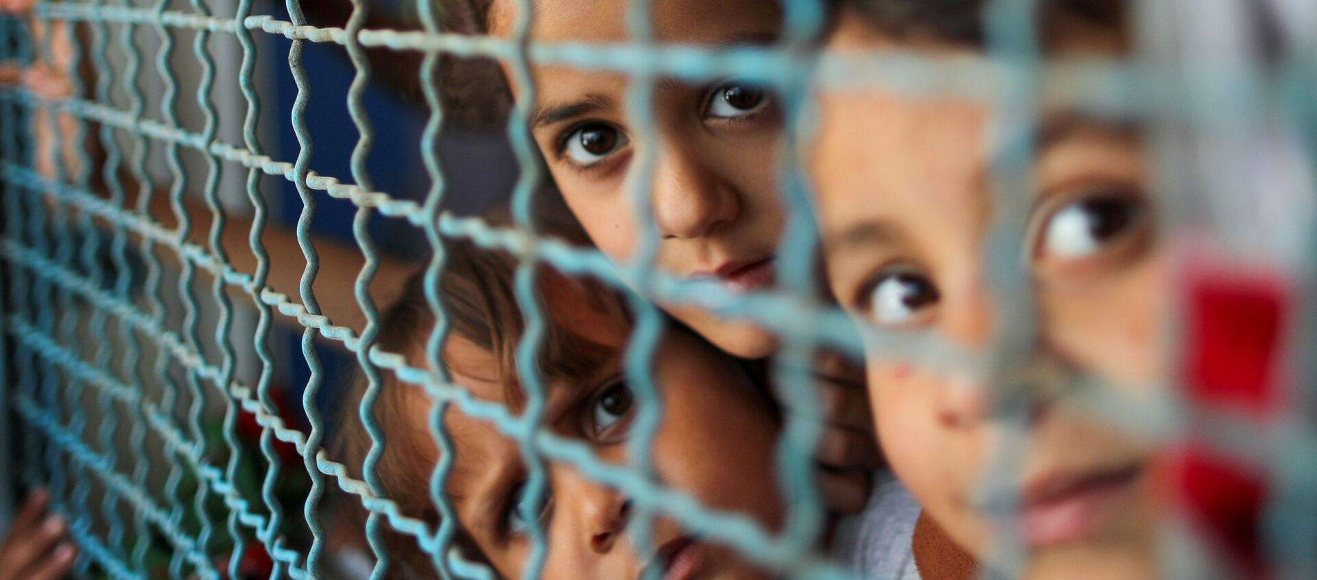 Trẻ em Palestine phải ra khỏi nhà bởi các cuộc không kích và pháo binh của Israel đang nhìn qua lan can cửa sổ của trường học do Liên hợp quốc điều hành, nơi họ trú ẩn ở thành phố Gaza - Sputnik Việt Nam, 1920, 04.06.2021
