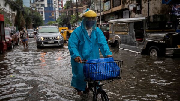 Một người đàn ông đeo mặt nạ đạp xe dọc con phố ngập lụt ở Manila, Philippines. - Sputnik Việt Nam
