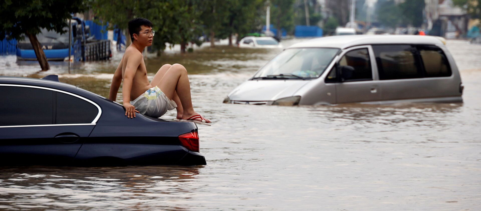Một người đàn ông ngồi trên ô tô mắc kẹt trên con đường ngập nước sau trận mưa lớn ở Trịnh Châu, tỉnh Hà Nam, Trung Quốс - Sputnik Việt Nam, 1920, 02.08.2021
