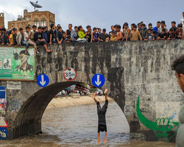 Đám thanh niên xem chàng trai nhảy từ cầu bắc qua kênh thoát nước ngập lụt ở thành phố cổ của thủ đô Yemen - Sputnik Việt Nam