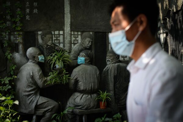 Người đàn ông đi qua các bức tượng đeo khẩu trang bên ngoài một nhà hàng ở Bắc Kinh - Sputnik Việt Nam