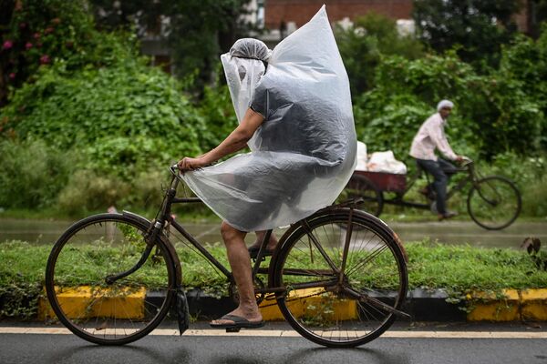 Một người đi xe đạp dùng túi nhựa che trong trận mưa ở Faridabad, Ấn Độ - Sputnik Việt Nam