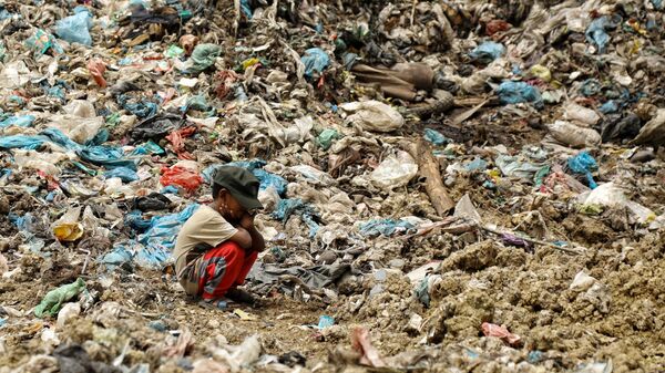 Con trai của một công nhân thu gom rác nghỉ ngơi trong khi người cha tìm kiếm đồ để bán lại tại một bãi rác ở Alue Liem, Lhokseumawe  - Sputnik Việt Nam
