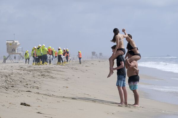 Trong bối cảnh những người thợ mặc đồ bảo hộ dọn sạch bãi biển ô nhiễm ở Huntington Beach, Hoa Kỳ - Sputnik Việt Nam