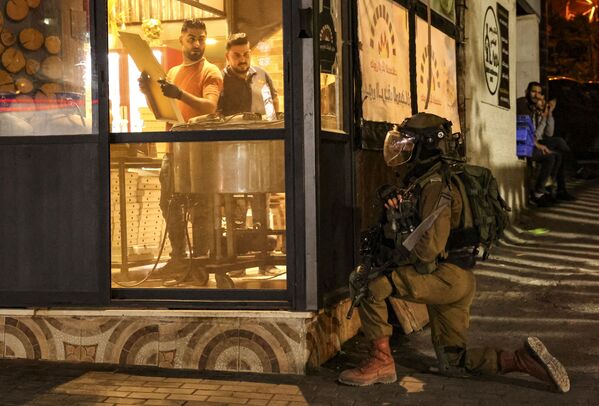 Những người thợ trong tiệm bánh nhìn một nhân viên an ninh Israel trong cuộc đụng độ với người biểu tình Palestine ở thành phố Hebron. - Sputnik Việt Nam