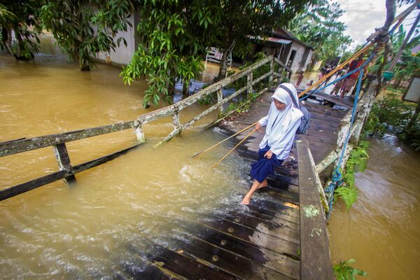 Cô gái đi qua một cây cầu bị phá hủy bị hư hỏng do lũ sông sau lũ lụt ở Indonesia - Sputnik Việt Nam