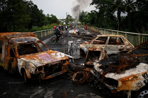 Người đàn ông đi xe đạp tránh chướng ngại vật được làm từ những chiếc ô tô bị cháy trên đảo Guadeloupe - Sputnik Việt Nam