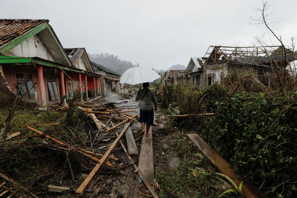 Người đàn ông cầm ô đứng giữa những ngôi nhà bị phá hủy trong vụ phun trào núi lửa Semeru ở Indonesia - Sputnik Việt Nam