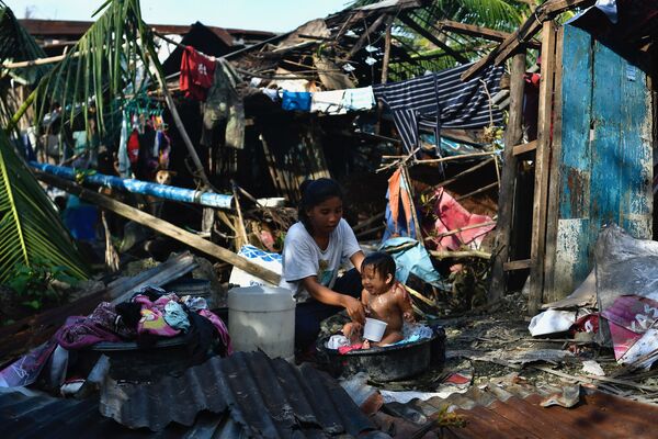 Cư dân tắm cho con bên cạnh ngôi nhà bị phá hủy ở Karkar, Philippines - Sputnik Việt Nam