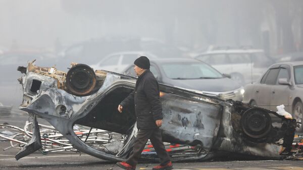 Người đàn ông đi ngang qua chiếc ô tô bị thiêu rụi sau cuộc biểu tình ở Almaty, Kazakhstan. - Sputnik Việt Nam