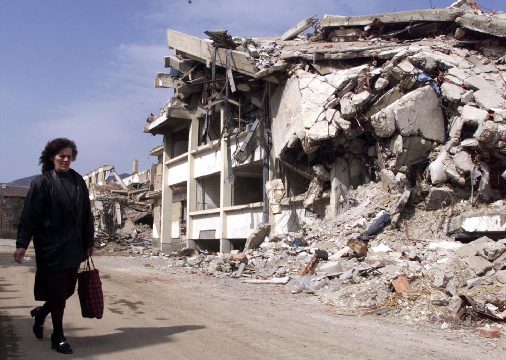 Người phụ nữ đi ngang qua tòa nhà ở Kosovska Mitrovica (Nam Tư) bị phá hủy bởi bom NATO, năm 1999 - Sputnik Việt Nam, 1920, 24.03.2022
