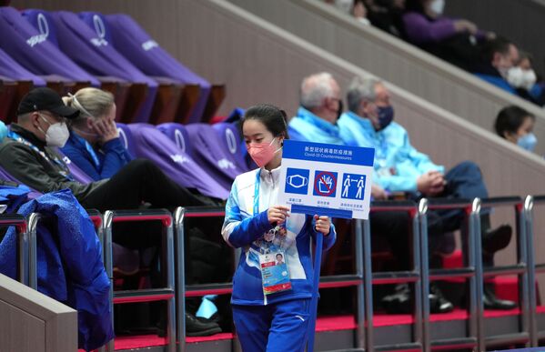 Tình nguyện viên cầm biển báo giữ khoảng cách và đeo khẩu trang tại sân vận động tổ chức các cuộc thi trượt băng nghệ thuật đồng đội tại Thế vận hội mùa đông Olympic lần thứ XXIV ở Bắc Kinh - Sputnik Việt Nam