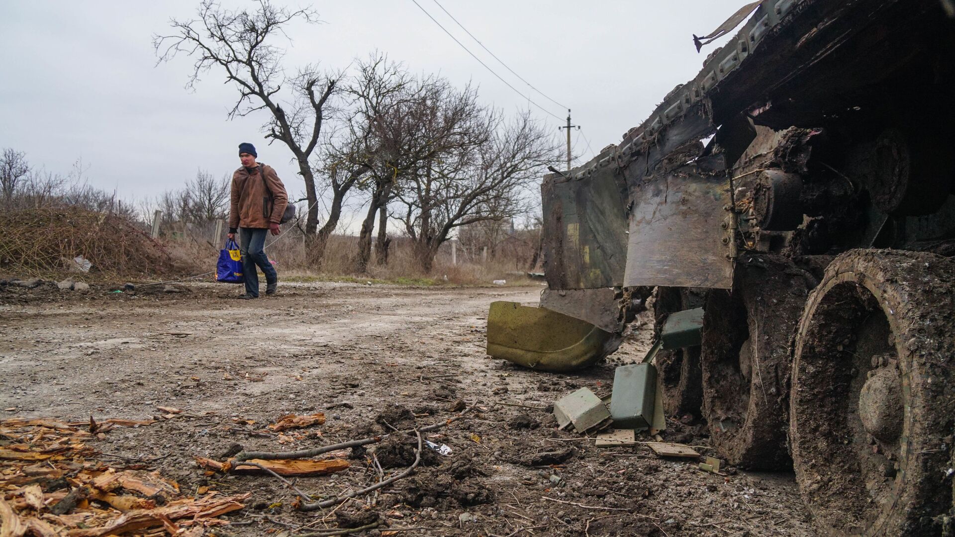 Một cư dân làng Gnutovo đi ngang qua chiếc xe tăng của quân đội Ukraina bị bắn cháy gần Mariupol - Sputnik Việt Nam, 1920, 20.03.2022