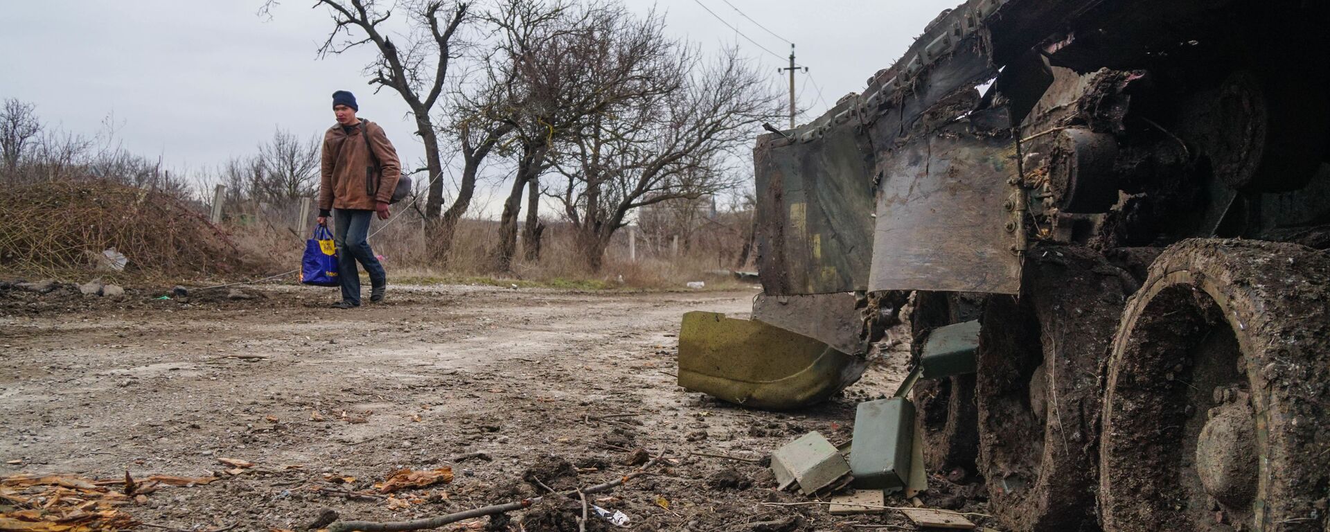 Một cư dân làng Gnutovo đi ngang qua chiếc xe tăng của quân đội Ukraina bị bắn cháy gần Mariupol - Sputnik Việt Nam, 1920, 06.03.2022