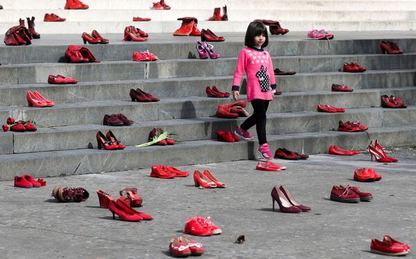 Bé gái ở Tirana (Albania) đứng giữa tác phẩm sắp đặt nhân ngày ngày 8/3, làm từ những chiếc giày phụ nữ màu đỏ, như một biểu tượng lên án bạo lực đối với phụ nữ - Sputnik Việt Nam