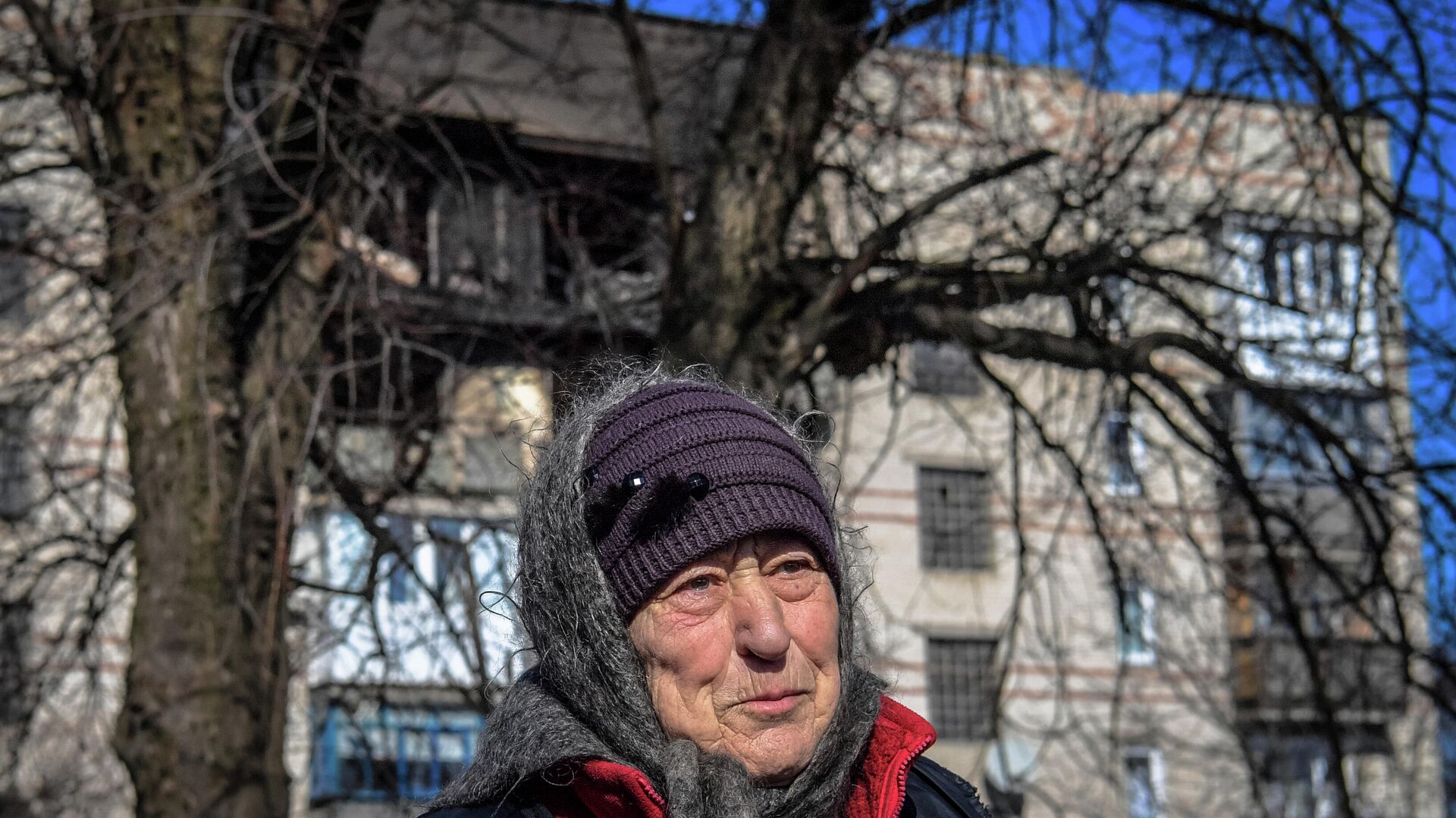 Hình ảnh một phụ nữ lớn tuổi trên nền một ngôi nhà bị hư hại do pháo kích ở thành phố Volnovakha^ Cộng hòa Nhân dân Donetsk, DNR - Sputnik Việt Nam, 1920, 14.03.2022