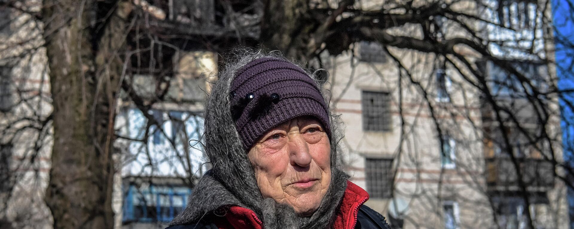 Hình ảnh một phụ nữ lớn tuổi trên nền một ngôi nhà bị hư hại do pháo kích ở thành phố Volnovakha^ Cộng hòa Nhân dân Donetsk, DNR - Sputnik Việt Nam, 1920, 14.03.2022