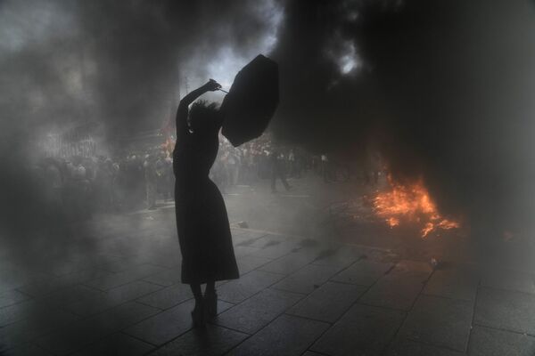 Người biểu tình với chiếc ô trong làn khói trong cuộc biểu tình phản đối việc tái cấu trúc khoản nợ 45 tỷ đô la ở Buenos Aires, Argentina - Sputnik Việt Nam