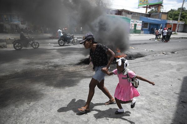 Người phụ nữ dắt đứa trẻ đi ngang qua cuộc biểu tình chống gia tăng bạo lực ở Port-au-Prince, Haiti - Sputnik Việt Nam