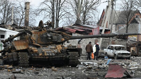 Người dân ở Volnovakha đi bộ về nhà qua một chiếc xe tăng của Lực lượng vũ trang Ukraina bị đắm. - Sputnik Việt Nam