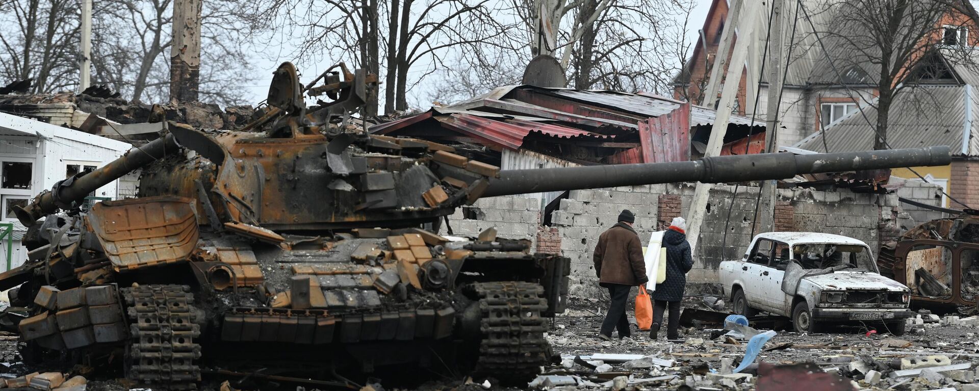 Người dân ở Volnovakha đi bộ về nhà qua một chiếc xe tăng của Lực lượng vũ trang Ukraina bị đắm. - Sputnik Việt Nam, 1920, 27.05.2022