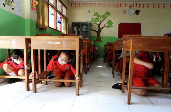 Học sinh nấp dưới bàn học của mình trong cuộc diễn tập động đất và sóng thần lớn ở Bali, Indonesia. - Sputnik Việt Nam