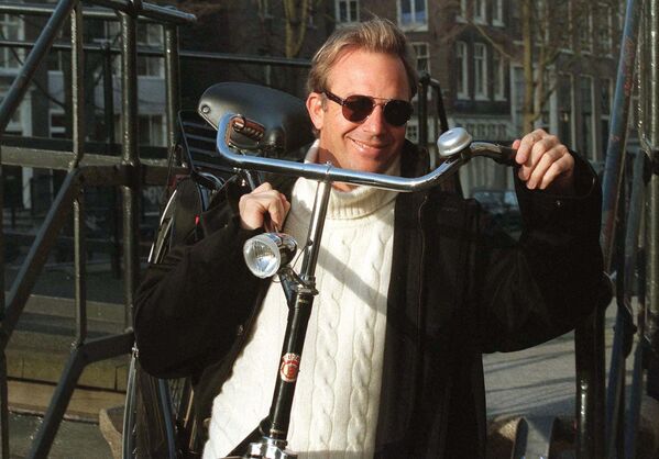 Nam diễn viên người Mỹ Kevin Costner cùng một chiếc xe đạp qua một cây cầu ở Amsterdam. - Sputnik Việt Nam