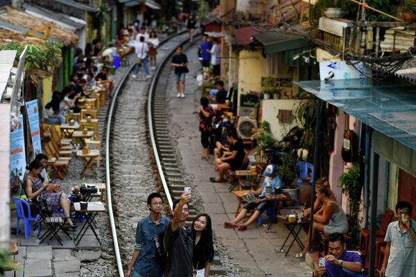 Nam thanh niên chụp ảnh tự sướng gần đoàn tàu chạy qua trong khu vực quán cà phê du lịch trên đường tàu Hà Nội. - Sputnik Việt Nam