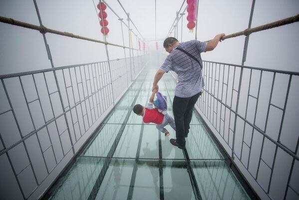 Một du khách Trung Quốc nắm tay con trai khi đi qua cây cầu treo sàn kính ở dãy núi Xinyuzhai, Trung Quốc. Ban đầu, cây cầu là một lối đi bằng gỗ dài khoảng 300m. - Sputnik Việt Nam