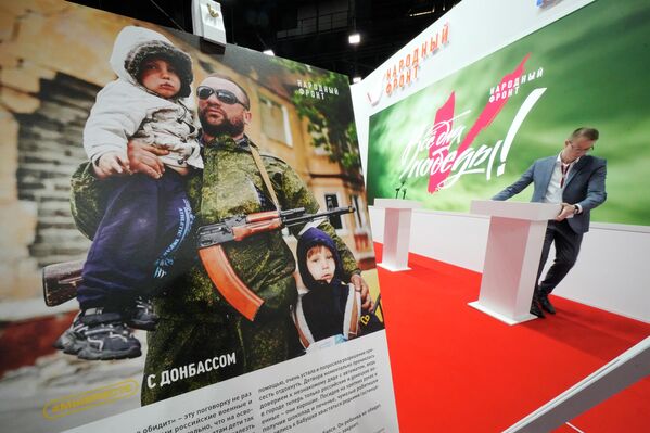 Người đàn ông đứng lên bục phát biểu của phong trào Mặt trận Nhân dân Nga với tấm áp phích mô tả một quân nhân Donbas với hai đứa trẻ. - Sputnik Việt Nam