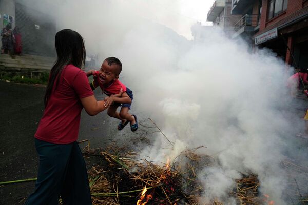 Người phụ nữ hơ con trai qua hình nộm quỷ Ghantakarna đang cháy, tượng trưng cho sự tiêu diệt cái ác, trong lễ hội Ghantakarna ở Bhaktapur, Nepal. - Sputnik Việt Nam