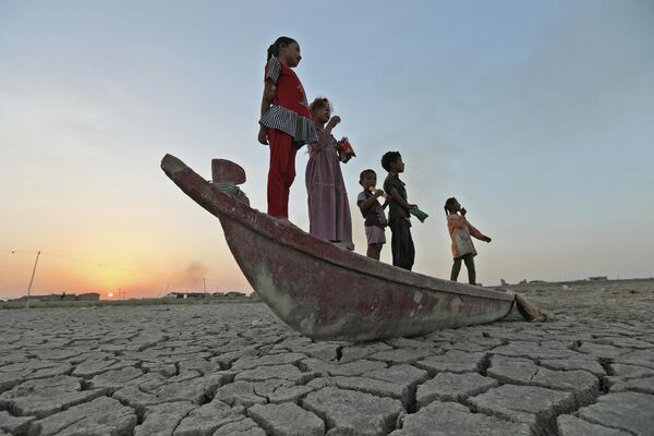 Trẻ em trên chiếc thuyền nằm trên đáy đầm lầy khô cạn Chibaish ở tỉnh Dhi Qar, Iraq. - Sputnik Việt Nam